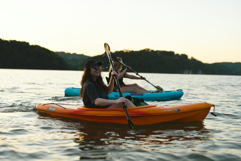Woman in blue shirt and blue denim jeans riding orange kayak on water during daytime
